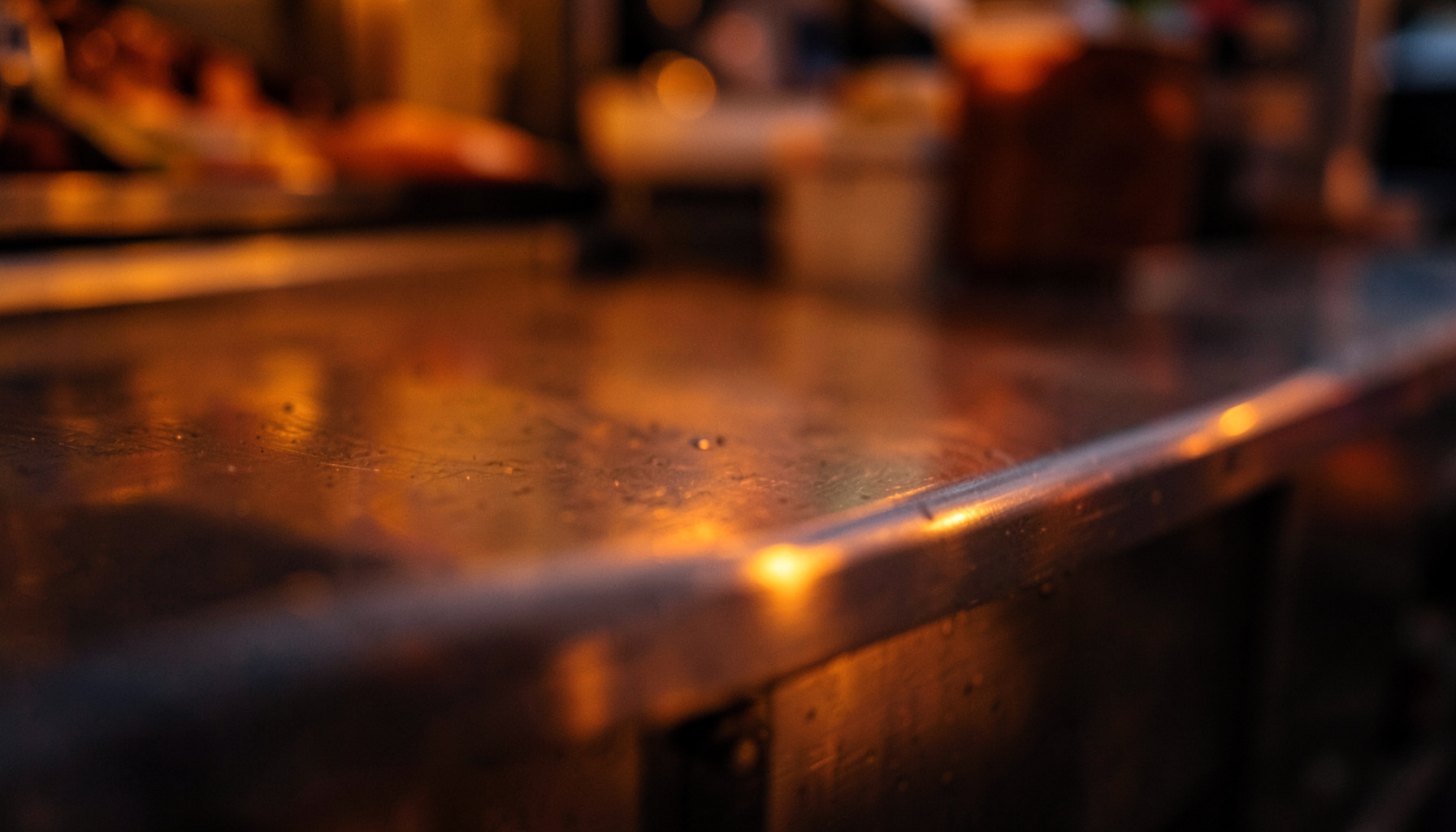 Warm close-up of a food truck's stainless steel counter at dusk, soft amber and deep brown tones