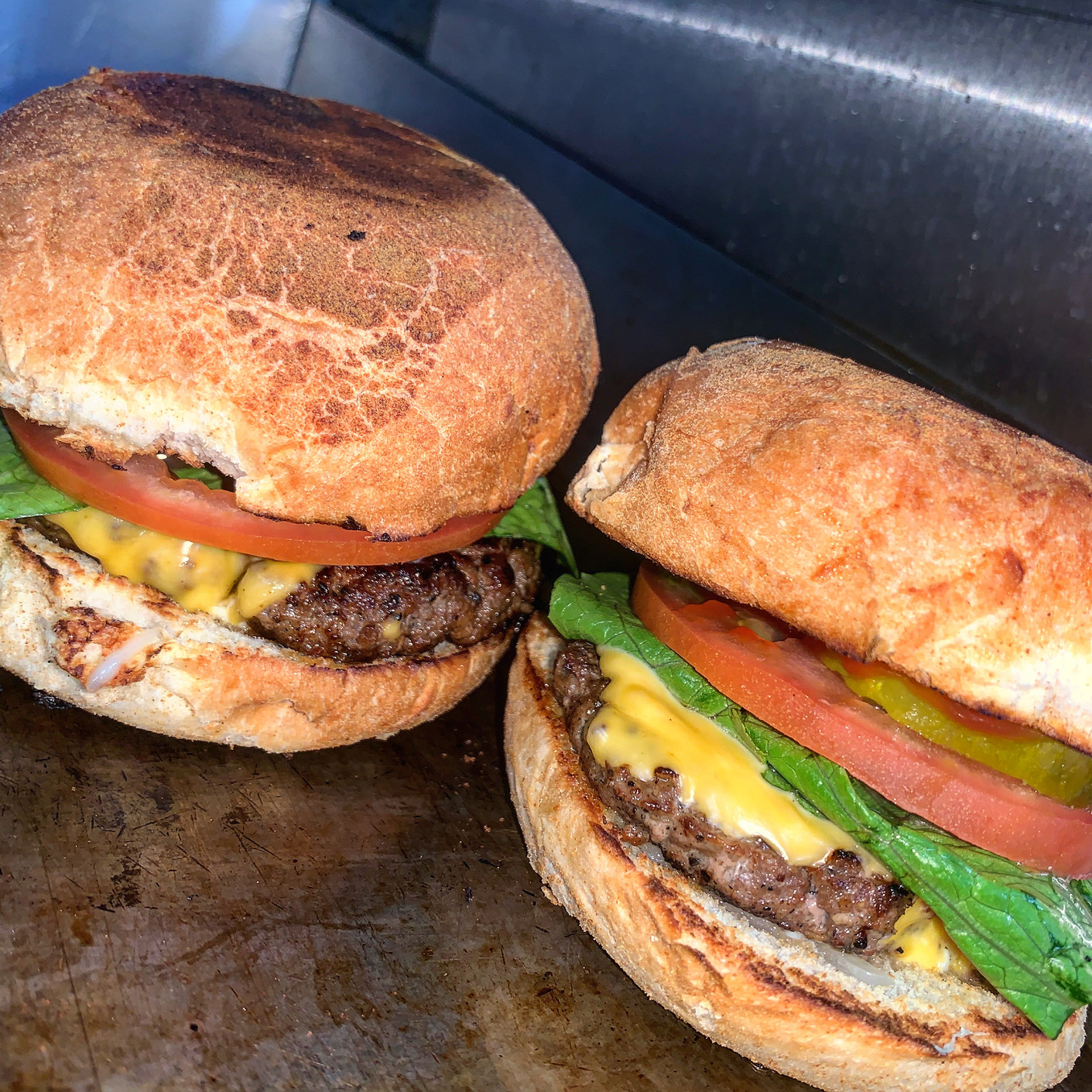 Two burgers with beef patties, cheese, lettuce, tomato, and pickles on toasted buns, warm lighting, appetizing close-up