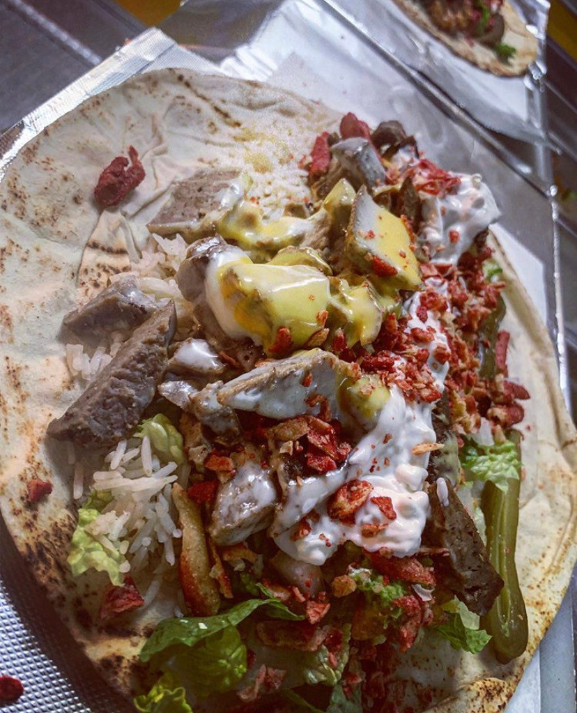 Close-up of a stuffed flatbread wrap filled with meat, rice, pickles, sauces and herbs in warm tones