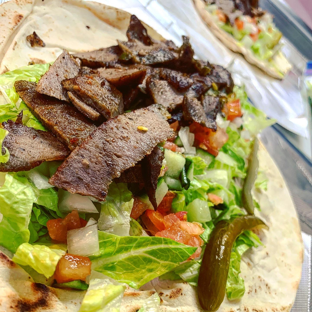 Close-up of a wrap filled with sliced grilled meat, lettuce, tomato, onion, and a pickle in warm tones