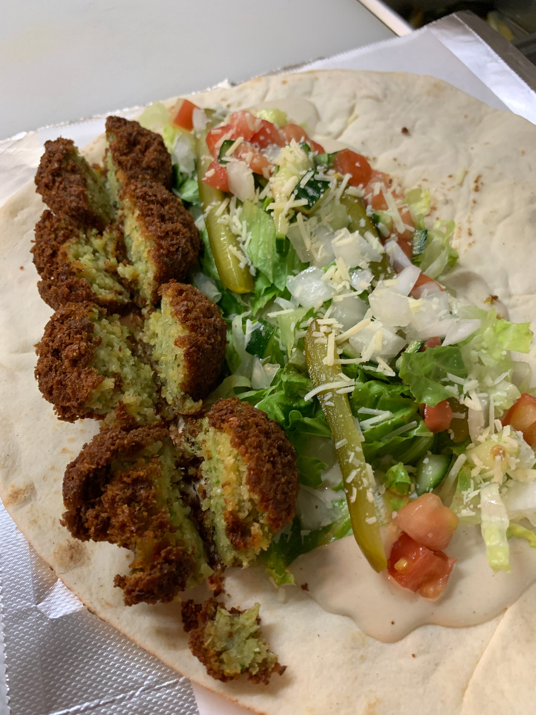 Top-down view of a flatbread wrap filled with fried falafel pieces, shredded lettuce, diced tomato, pickles and onions