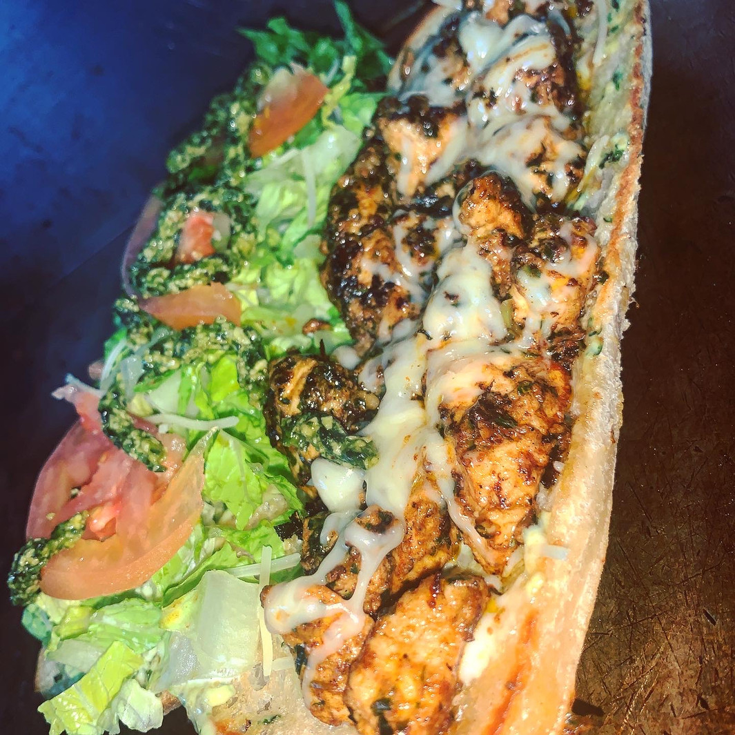 Close-up of a sandwich with grilled chicken pieces, melted cheese, lettuce and tomato, warm lighting