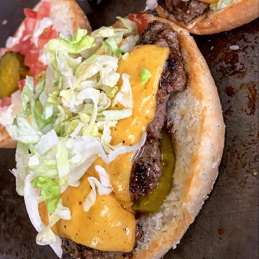Close-up of a burger with beef patty, melted cheese, pickles, shredded lettuce and bun